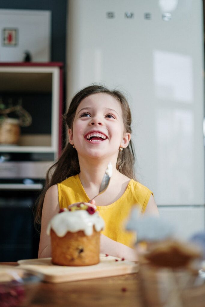 girl in yellow shirt holding spoon with icing