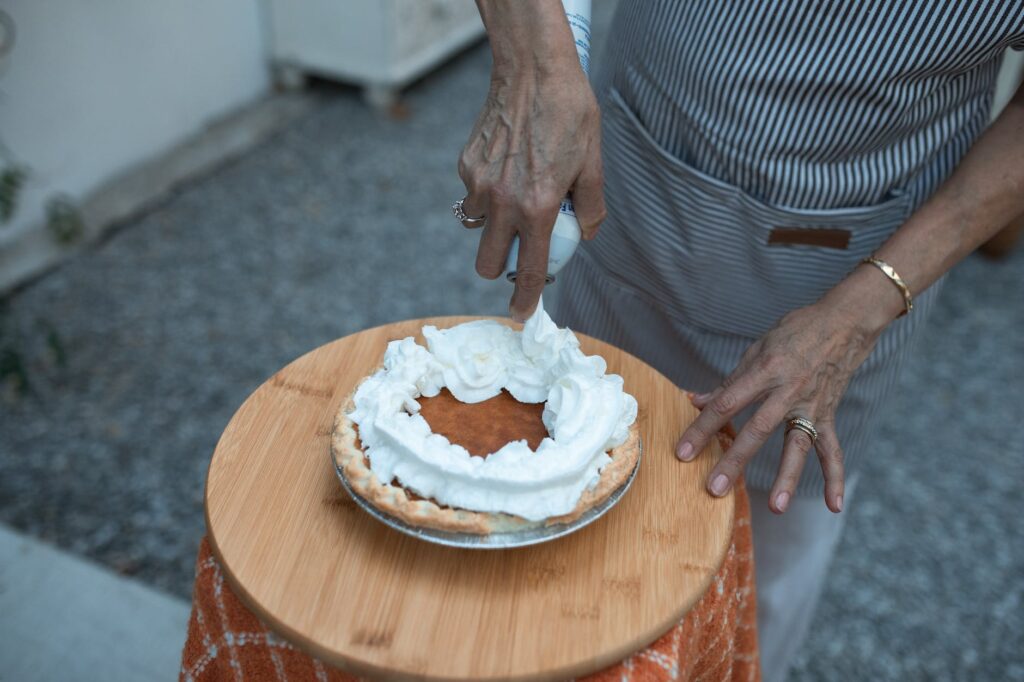 person putting icing on baked pumpkin pie